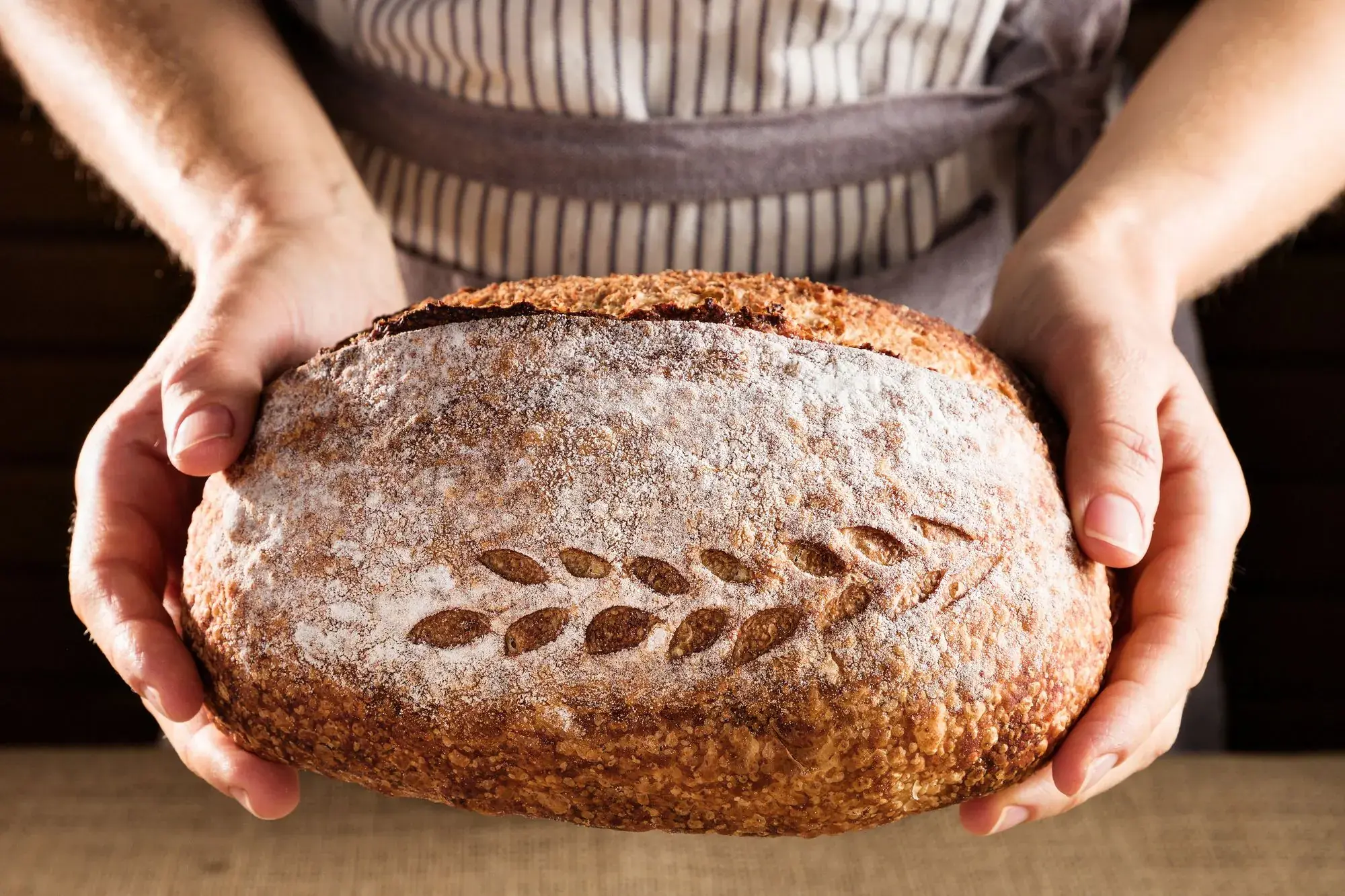 A scored sourdough loaf held in two hands