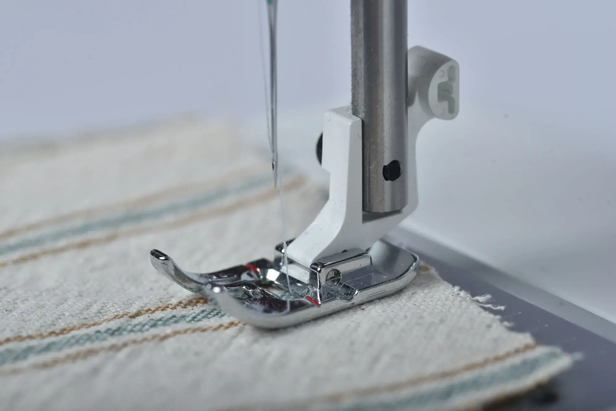 A sewing machine needle stitching striped cotton