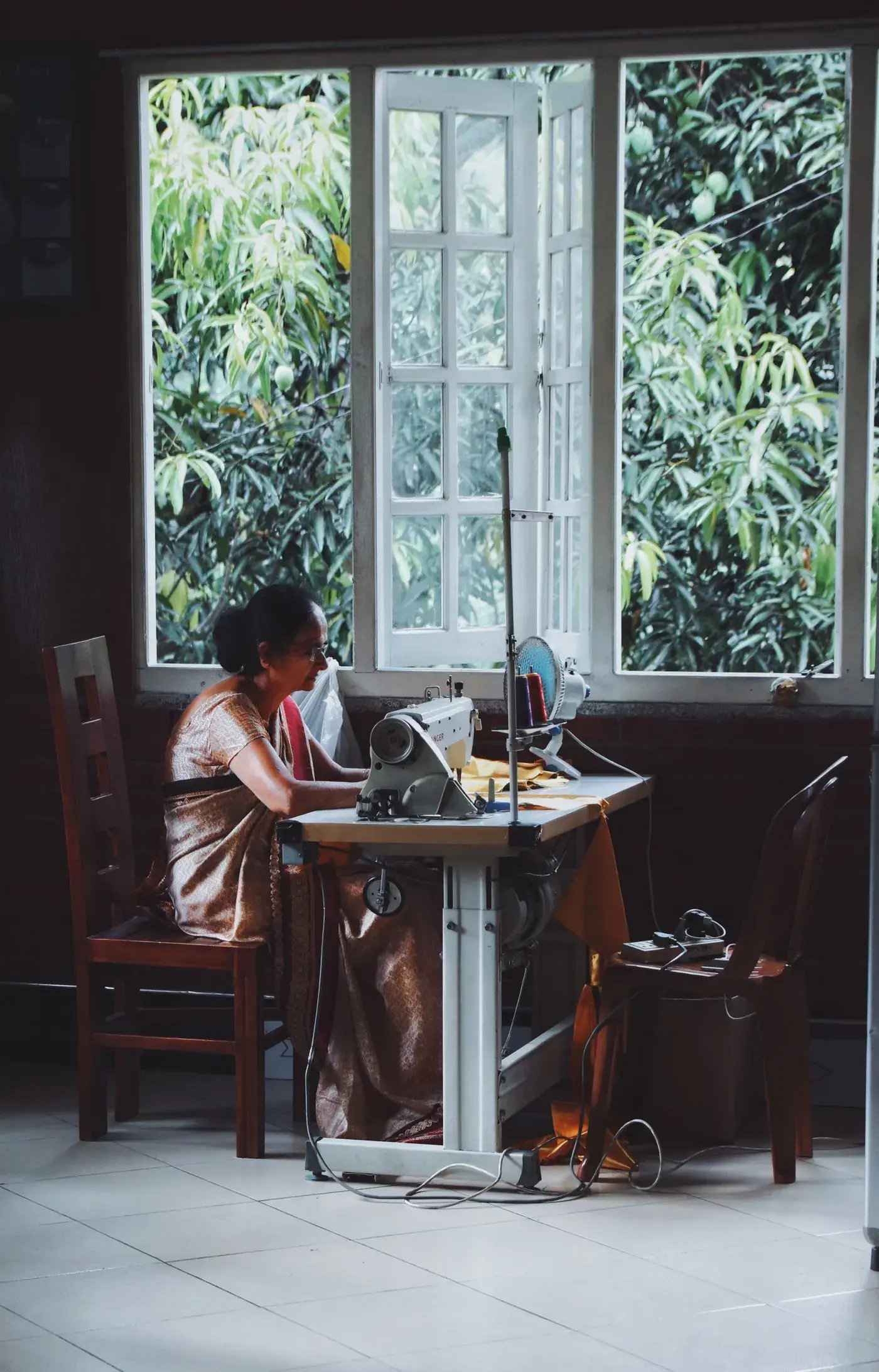 A tailor at her sewing machine beside a window